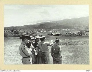 WAU, NEW GUINEA. 1944-04-25. MAJOR-GENERAL B.M. MORRIS, DSO, GOC AUSTRALIAN NEW GUINEA ADMINISTRATIVE UNIT (1), INDICATES AN AUSTRALIAN ARMY BRIGADE REST CAMP AT THE REAR OF WAU AIRFIELD TO THE ..