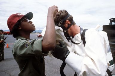 AIRMAN 1ST Class Tanya Jenkins, a bio-environmental specialist from the Hickam Clinic, helps a toxic-vapor detection member put on a face mask. They are participating in a space shuttle emergency landing exercise