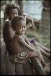 Children sit on house veranda, Imala (girl in front) wears a red shell necklace