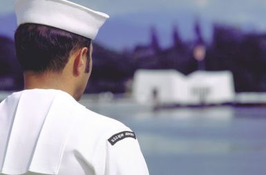 A sailor stands at attention as the battleship USS NEW JERSEY (BB-62) passes the USS ARIZONA Memorial