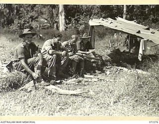YAULA, NEW GUINEA. 1944-04-09. MEMBERS OF THE 2ND MOUNTAIN BATTERY, READING MAIL AND CLEANING WEAPONS OUTSIDE A MAKESHIFT HUT CONSTRUCTED WITH A ROOF TOP OF BANANA LEAVES. THE UNIT IS ENGAGED IN ..