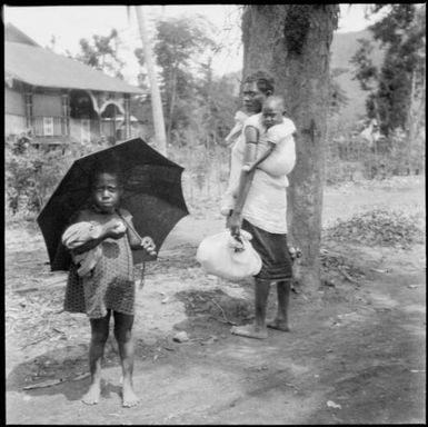 Woman with a child on her back and an infant holding an umbrella, New Guinea, ca. 1936 / Sarah Chinnery