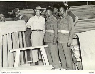 ALEXANDRIA, NSW. 1944-01-24. AUSTRALIAN AND NEW GUINEA ADMINISTRATION UNIT NATIVES BEING SHOWN HEAVY STRUCTURAL WOODEN LAMINATIONS FOR ASSAULT BARGES AT SLAZENGER'S FACTORY