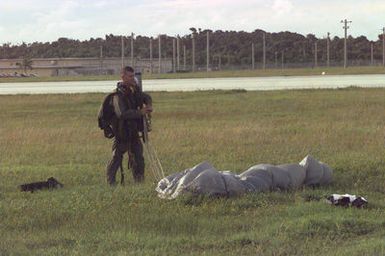 Right side front view medium shot of US Marine STAFF Sergeant Pitchford, Company Gunny Sergeant from Headquarters and Service Company, 5th Reconnaissance Battalion, 3rd Marine Division, as he gathers up his MC5 parachute after successfully jumping from a US Air Force C-141 Starlifter (Not shown) during the Force Reconnaissance Exercises at Andersen Air Force Base, Guam