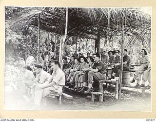 WUNUNG, JACQUINOT BAY, NEW BRITAIN, 1945-08-25. SPECTATORS IN THE SPECIAL GRANDSTAND AT THE ALLIED INTELLIGENCE BUREAU SING-SING TO MARK THE END OF HOSTILITIES. AUSTRALIAN ARMY NURSING SERVICE ..