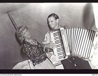 TOROKINA, BOUGAINVILLE, 1945-11-03. PRIVATE G. J. BUCKHAM, FEMALE IMPERSONATOR, AND CORPORAL A. M. RONEY, ACCORDIONIST, MEMBERS OF THE KOOKAROOS CONCERT PARTY, AUSTRALIAN ARMY AMENITIES SERVICE, ..