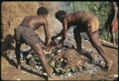 Two men laying pork out on the stone oven