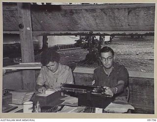 LAE, NEW GUINEA. 1945-05-15. CORPORAL O. TAYLOR (1), AT THE CAMP COMMANDANT'S OFFICE, HEADQUARTERS FIRST ARMY, RECEIVING INSTRUCTIONS IN HER CLERICAL DUTIES FROM CORPORAL A.B. CUNNINGHAM (2). A FEW ..