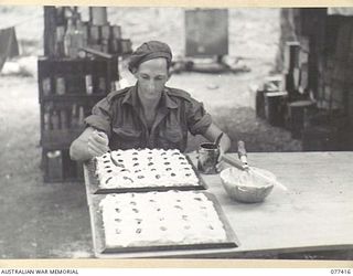 MALMAL MISSION, JACQUINOT BAY, NEW BRITAIN. 1944-11-30. Q100267 PRIVATE V. NETTLE, COOK, HEADQUARTERS, 5TH DIVISION, WITH A BATCH OF CAKES ALMOST READY FOR THE OVEN