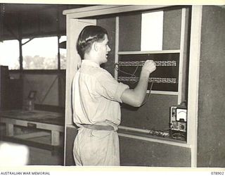 LAE, NEW GUINEA. 1945-02-06. VX74625 SIGNALLER E.H. FREDRICKSON, 19TH LINES OF COMMUNCIATION SIGNALS, HEADQUARTERS, FIRST AUSTRALIAN ARMY, PATCHING KEYING LINES FROM THE PATCH PANEL AT THE MAIN ..