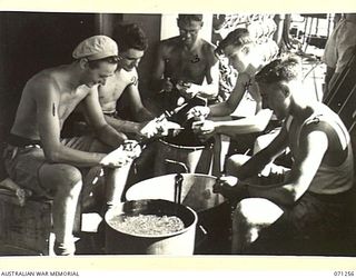 AT SEA, 1944-03. THESE "SPUD BARBERS", PEELING POTATOES ABOARD HT TAROONA, ARE NAVAL PERSONNEL TRAVELLING FROM TOWNSVILLE, QUEENSLAND, TO MILNE BAY TO JOIN THEIR SHIP. IDENTIFIED PERSONNEL ARE: ..