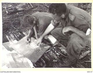 KIARIVU, NEW GUINEA, 1945-08-09. CAPTAIN G.E. DUFFY (2) AND SERGEANT S. FYFE (1), MEMBERS OF 2/7 INFANTRY BATTALION, MARKING ON THE MAP THE VARIOUS POSITIONS OCCUPIED BY THE BATTALION IN THE AREA