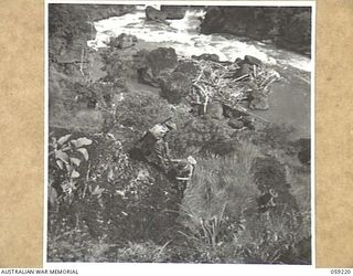 LALOKI VALLEY, NEW GUINEA, 1943-11-05. ONE MEMBER OF THE PATROL OF THE NEW GUINEA FORCE TRAINING SCHOOL (JUNGLE WING) LOWERING ANOTHER, BY MEANS OF A RIFLE, OFF A ROCKY LEDGE TO THE BANK OF THE ..