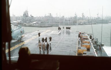 Crew members aboard the amphibious assault ship USS GUAM (LPH-9) brave the rain to watch from the flight deck as the ship approaches its berth at the naval station. The GUAM is returning to Naval Station, Norfolk, Va., following its deployment to the Persian Gulf region for Operation Desert Shield and Operation Desert Storm