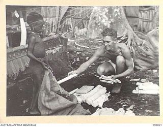 MOROKAIMORO, BOUGAINVILLE, 1945-06-06. TROOPER A.H. DARK, 2/8 COMMANDO SQUADRON, ASSISTED BY A PICCANINNY FROM THE AREA, SORTS SQUADRON MAIL, WHICH HAS BEEN DROPPED BY AIR