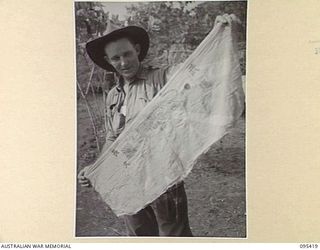 KIARIVU, NEW GUINEA, 1945-08-14. WARRANT OFFICER 2 T. HEALEY, AUSTRALIAN NEW GUINEA ADMINISTRATIVE UNIT REPRESENTATIVE IN KIARIVU WITH HIS CAPTURED JAPANESE FLAG. THE FLAG, KNOWN AS THE FLAG WITH A ..