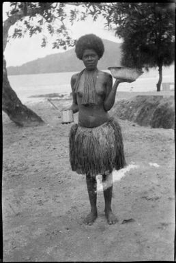 Woman wearing a grass skirt holding a dish and a tin, New Guinea, ca. 1936 / Sarah Chinnery