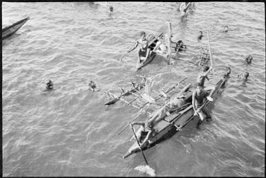 Looking down onto two outrigger canoes with several people swimming, Rabaul Harbour, New Guinea, ca. 1929 / Sarah Chinnery