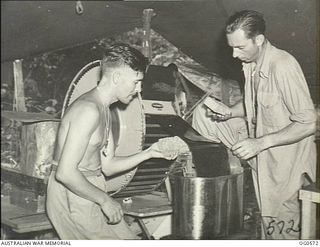 MILNE BAY, PAPUA. 1943-07-31. LEADING AIRCRAFTMAN (LAC) H. HARDIE, KOGARAH, NSW (RIGHT) DRYING FILM WITH HOT AIR WHILE LAC K. W. GILL, SYDNEY, NSW, WIPES SURPLUS MOISTURE OFF THE FILM WITH A ..