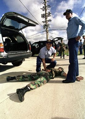 US Navy Personnelman 3rd Class (PN3) Zikomo S. Bullock (left) and Electronics Technician 3rd Class (ET3) Marvin T. Marsh, USN, (right) "apprehend" Crytologic Technician SEAMAN (CTSN) Martin Quackenbush, USN, as a suspected bomb smuggler during a demonstration of vehicle search techniques. Agana Naval Air Station, Guam, 8 May 1998