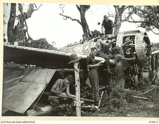 DAGUA, NEW GUINEA. 1945-03-25. MEMBERS OF NO.10 PLATOON, B COMPANY, 2/2 INFANTRY BATTALION ALONGSIDE THEIR "DOOVER" (SHELTER) UNDER THE WING OF A WRECKED JAPANESE AIRCRAFT ON THE AIRSTRIP. ..