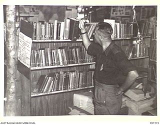 CAPE WOM, NEW GUINEA. 1945-09-29. WARRANT OFFICER 2 W.R. DUNN, HEADQUARTERS 6 DIVISION, SELECTING A BOOK FROM THE LIBRARY. THE LIBRARY IS RUN BY THE AUSTRALIAN ARMY EDUCATION SERVICE AND CONTAINS ..