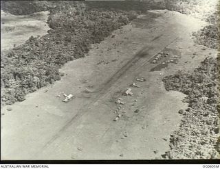 New Guinea. C. 1944. Aerial photograph of an airfield runway, with aircraft parked in front of the tree-line
