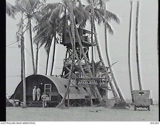 TOROKINA, BOUGAINVILLE. 1945-03-01. THE NAVAL BASE HEADQUARTERS CONSISTING OF A QUONSET HUT AND LOOKOUT TOWER AMONGST TALL PALM TREES. (NAVAL HISTORICAL COLLECTION)