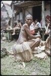 Mortuary ceremony: mourning woman with shaved head wearing long fiber skirt, she arranges banana leaf bundles for exchange