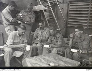 AT SEA IN THE ADMIRALTY ISLANDS AREA. 1944-03-18. THERE ARE NO OFFICERS' MESS COMFORTS ON CROWDED LANDING CRAFT. RAAF OFFICERS EATING THEIR LUNCH ON DECK ARE: FLYING OFFICER (FO) L. B. SODEN, ..