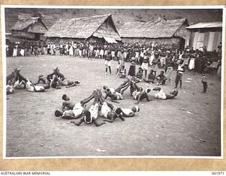 KILA KILA, PAPUA, NEW GUINEA. 1943-12-25. KEREMA BOYS EXECUTING A DANCE AT THE AUSTRALIAN AND NEW GUINEA ADMINISTRATION UNIT NATIVE LABOUR CAMP. THE DANCERS WEAR LONG TRAILS OF GRASS AND FLOWERS, ..