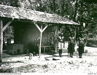 THE SOLOMON ISLANDS, 1945-10-12. THREE NATIVES OUTSIDE A FORMER JAPANESE WORKSHOP ON BOUGAINVILLE ISLAND. (RNZAF OFFICIAL PHOTOGRAPH.)
