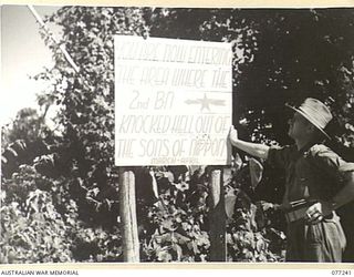 TOROKINA, BOUGAINVILLE ISLAND, 1944-12-24. NX201 MAJOR H.E. GALE, MBE, CAMP COMMANDANT, HEADQUARTERS, 2ND AUSTRALIAN CORPS, READING A NOTICE IN THE UNIT AREA. WHICH READS:- "YOU ARE NOW ENTERING ..