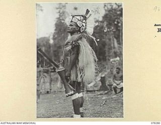 KAMALGAMAN ANCHORAGE, NEW BRITAIN. 1944-12-31. A MEMBER OF THE ROYAL PAPUAN CONSTABULARY DRESSED IN HIS NATIVE FINERY WAITING FOR HIS TURN TO DANCE DURING THE NATIVE SING-SING AT THE AUSTRALIAN AND ..