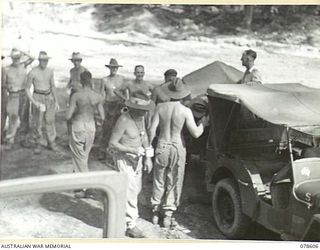 BOUGAINVILLE ISLAND. 1945-01-22. TROOPS OF THE 2/2ND FORESTRY UNIT LINE UP FOR MORNING TEA AT THE JOINT YOUNG MEN'S CHRISTIAN ASSOCIATION - AUSTRALIAN COMFORT FUND JEEP AND TRAILER IN THE 5TH BASE ..
