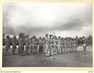 TOROKINA, BOUGAINVILLE. 1945-10-06. THE GUARD OF HONOUR DRAWN FROM 24 INFANTRY BATTALION PRESENT ARMS AT THE SOUNDING OF THE LAST POST DURING THE COMMEMORATIVE SERVICE IN THE TOROKINA WAR CEMETERY ..