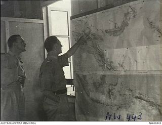 Darwin, NT. 1943. A RAAF officer in the Operations Room at North-West Area points out a feature on the New Guinea coast on a wall map to Air Commodore F. M. Bladin (left), Air Officer Commanding ..