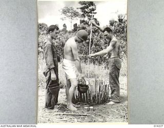 1943-01-26. PAPUA. NEARING THE END OF THE PAPUAN CAMPAIGN AGAINST JAPAN. TIN HATS ARE PUT TO MANY USES IN THE ARMY. HERE AN AMERICAN HAS GIVEN HIS TO ANOTHER TO HOLD AS HE FILLS IT FROM A FRESHLY ..