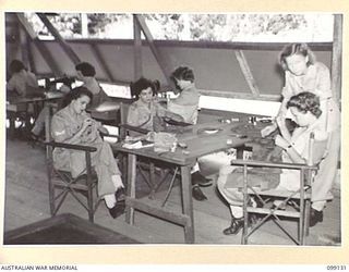 LAE, NEW GUINEA. 1945-11-25. SERGEANT CRAWFORD, (STANDING) GIVING NEEDLEWORK INSTRUCTIONS DURING THE DRESSMAKING CLASS HELD AT LAEWAS COLLEGE, AWAS BARRACKS, LAE. IDENTIFIED PERSONNEL ARE: SERGEANT ..