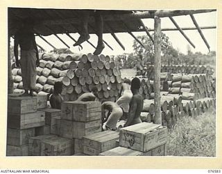 HOSKINS, NEW BRITAIN. 1944-10-10. NEW BRITAIN NATIVES STACKING DRUMS OF FLOUR, SUGAR AND OATMEAL AT THE AUSTRALIAN ARMY SERVICE CORPS DEPOT AT ONE OF THE 36TH INFANTRY BATTALION BRIDGEHEADS