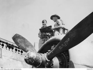 KIRIWINA, TROBRIAND ISLANDS, PAPUA. C. 1943-12. WING COMMANDER J. G. EMERTON, THE COMMANDING OFFICER OF NO. 22 (BOSTON) SQUADRON RAAF, STANDING IN THE COCKPIT, SIGNS THE AIRCRAFT HISTORY SHEET FORM ..