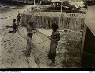 Yule Island, New Guinea. c. 1944-05-15. Private J. Fullarton known as "Mangrove Jack" repairing fishing nets with his native boys at the camp of 1 Marine Food Supply Platoon. In the background is ..