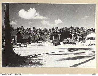 JACQUINOT BAY, NEW BRITAIN. 1945-06-09. THE MAIN TRUCK ENTRY TO ALL ORDNANCE STORES AT HEADQUARTERS 5 BASE SUB-AREA, SHOWING TRUCK DISPERSAL AREA AND STORAGE SHEDS