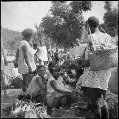 Woman, with a bilum hanging from her forehead, several women seated, Boong, native market, Rabaul, New Guinea, ca. 1936 / Sarah Chinnery