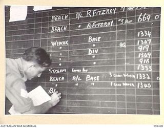 AITAPE BEACH HEAD, NEW GUINEA. 1945-06-19. SERGEANT I.M. STOCKDALE, 7 DOCKS OPERATING COMPANY, ROYAL AUSTRALIAN ENGINEERS, ENTERING ON A CHART WHICH CONTROLS MOVEMENTS OF ALL SHIPPING IN THE PORT; ..