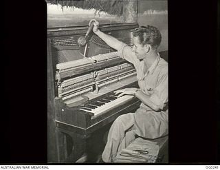 NEW GUINEA. C. 1943-12-21. LEADING AIRCRAFTMAN C. LOGAN WHO IS A BULLDOZER DRIVER IN A RAAF UNIT, TUNING A PIANO IN HIS SPARE TIME