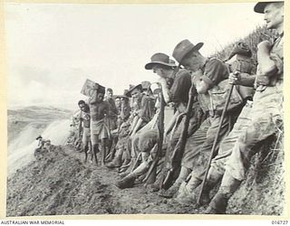 1944-03-23. NEW GUINEA. NATIVE CARRIERS BRING FORWARD SUPPLIES AS AN AUSTRALIAN UNIT RESTS ON THE FIRST STAGES OF THE TREK THROUGH THE TOUGH FINISTERRE RANGES ON THE TRACK TO JAPANESE-HELD BOGADJIM