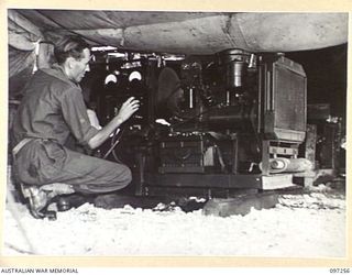 CAPE WOM, NEW GUINEA. 1945-09-29. SIGNALMAN R.W. ADAMS, INSTRUMENT MECHANIC, MAINTAINING A UNIT AT THE ARMY RADIO STATION ESTABLISHED IN THE UNIT LINES OF HEADQUARTERS 6 DIVISION. THE CHARGING IS ..