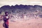 Man at exchange ceremony, earth ovens and food display in background