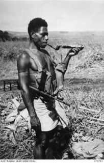 KELANOA, NEW GUINEA. 1944-03-04. 417 SERGEANT WILLIAM MATPI, A MEMBER OF "A" COMPANY, 1ST PAPUAN INFANTRY BATTALION, PICTURED LIGHTING HIS PIPE WITH A PIECE OF WOOD FROM THE FIRE. MATPI, WHO COMES ..
